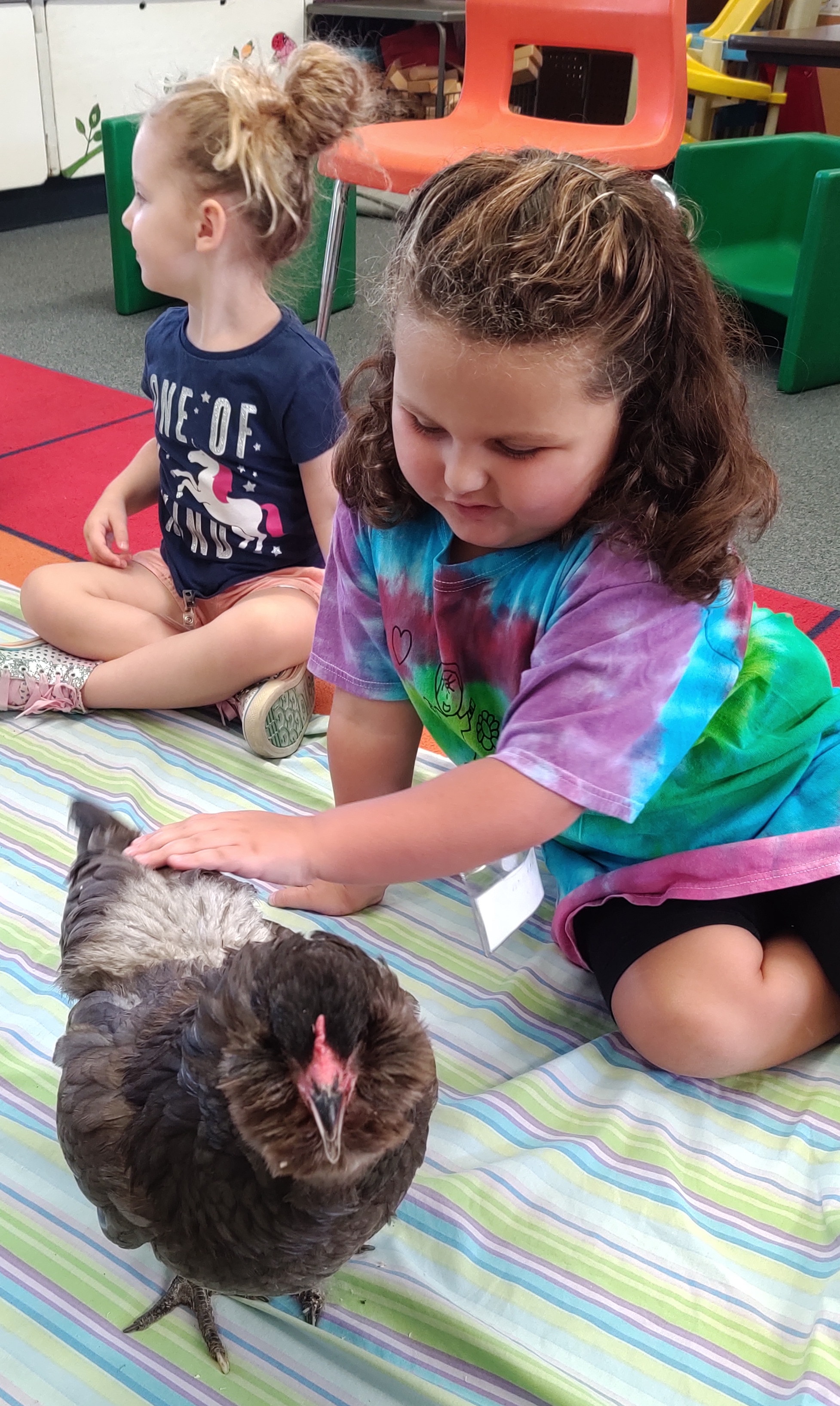 Two girls one is petting a visiting chicken.